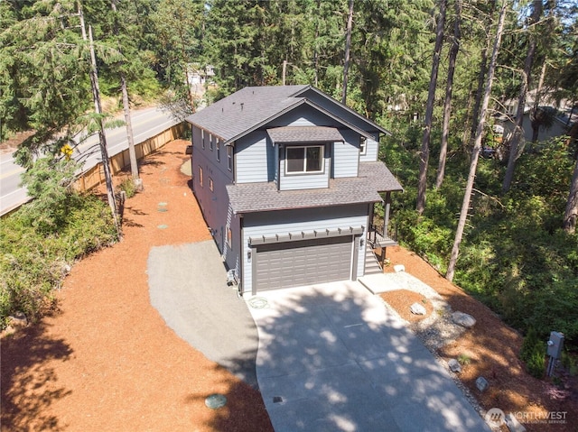 view of front of house with concrete driveway, roof with shingles, an attached garage, and fence