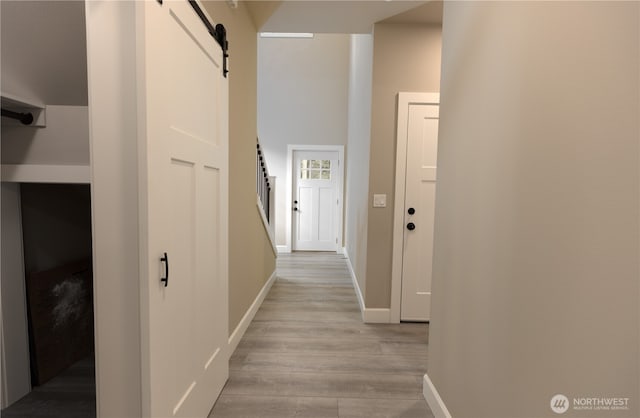 hallway with light wood-style floors, stairway, baseboards, and a barn door