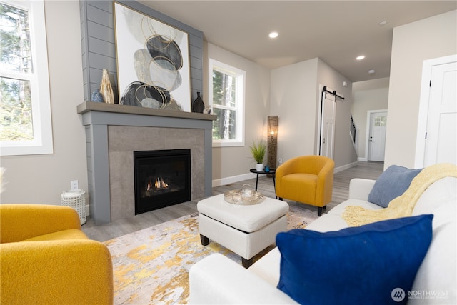 living room featuring a barn door, a tiled fireplace, light wood-style flooring, and recessed lighting