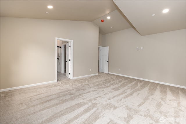 empty room featuring lofted ceiling, light carpet, baseboards, and recessed lighting