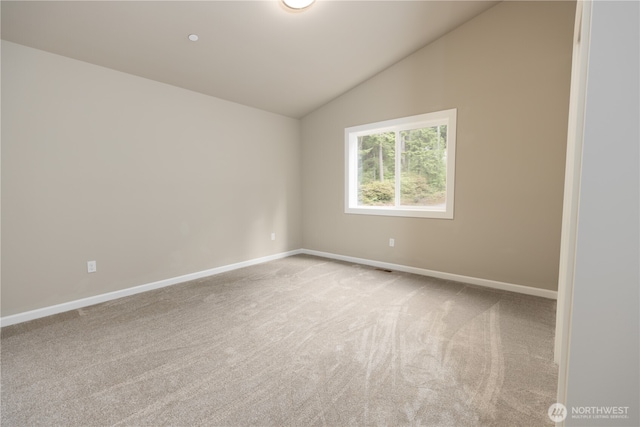 empty room with vaulted ceiling, baseboards, and light colored carpet