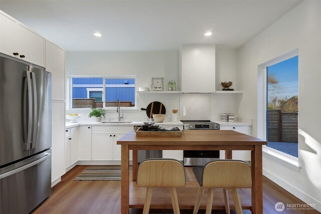 kitchen featuring open shelves, a sink, dark wood-style floors, appliances with stainless steel finishes, and wall chimney exhaust hood