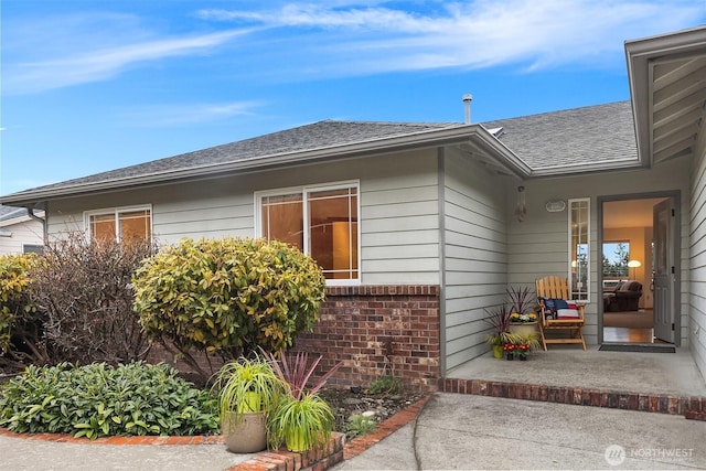 property entrance featuring a shingled roof and brick siding