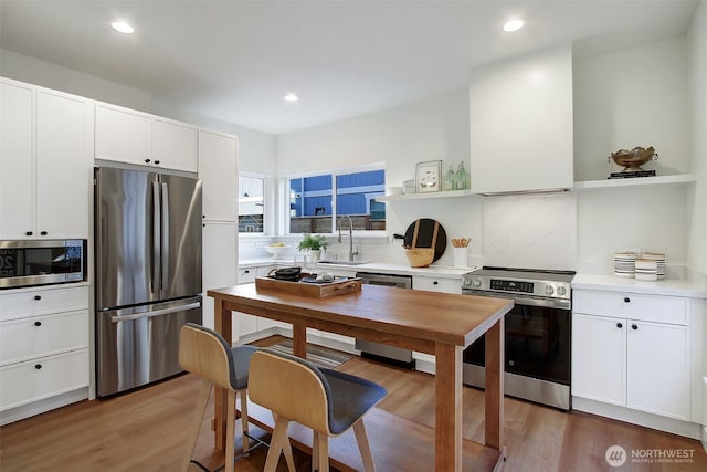 kitchen with light wood finished floors, open shelves, a sink, light countertops, and appliances with stainless steel finishes