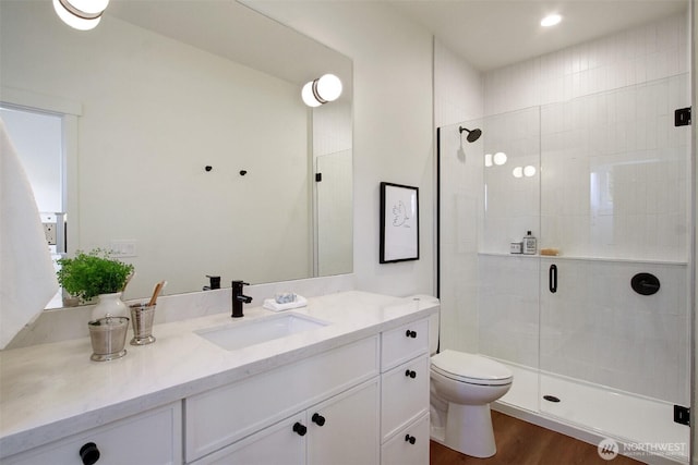 bathroom with vanity, toilet, wood finished floors, and a stall shower