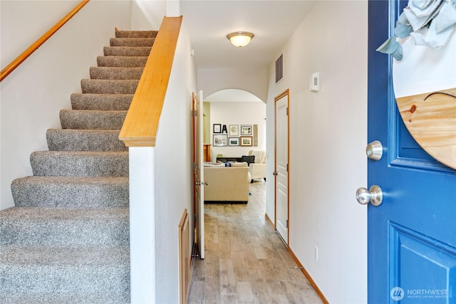 stairs with arched walkways, visible vents, and wood finished floors