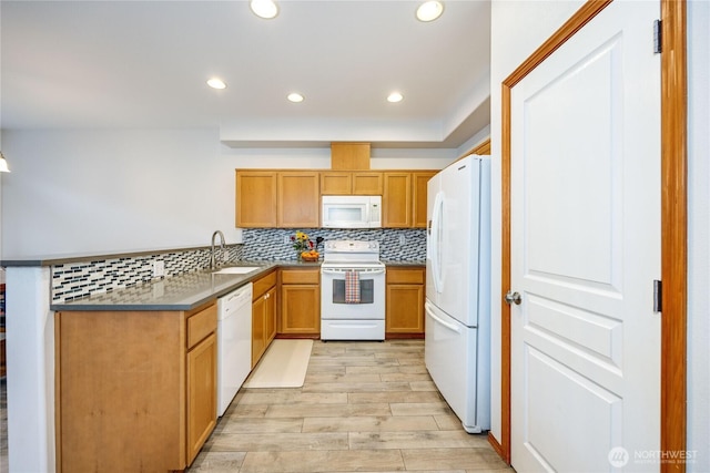 kitchen with light wood finished floors, backsplash, a sink, white appliances, and a peninsula