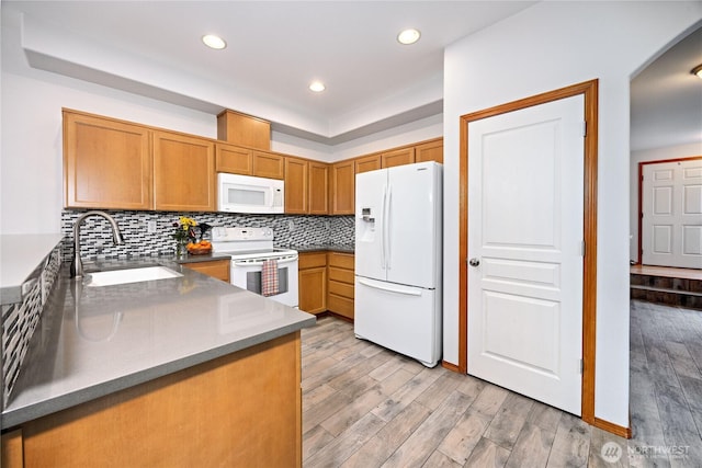 kitchen with white appliances, brown cabinetry, light wood-style flooring, a sink, and backsplash