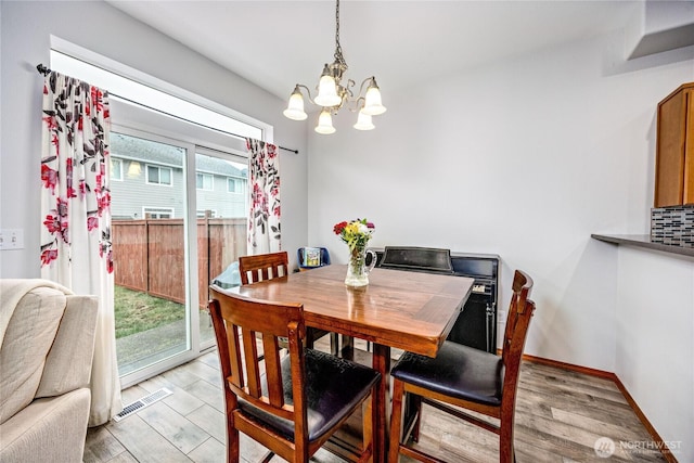 dining room featuring baseboards, visible vents, light wood finished floors, and an inviting chandelier