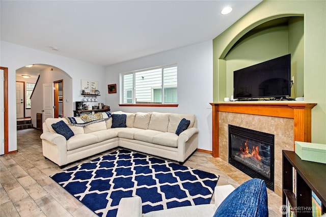 living room featuring arched walkways, recessed lighting, wood finished floors, a tile fireplace, and stairs