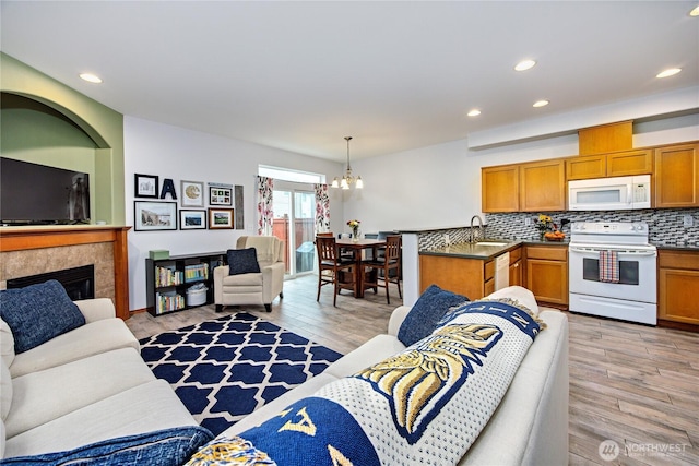 living area with a tile fireplace, light wood-style flooring, an inviting chandelier, and recessed lighting