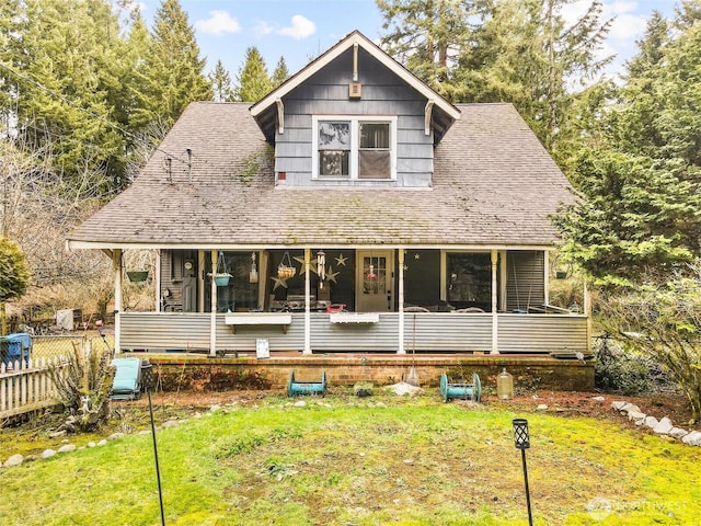 view of front of house featuring a porch, roof with shingles, fence, and a front lawn