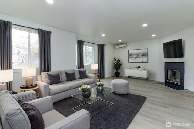 living area with a fireplace with flush hearth, an AC wall unit, recessed lighting, light wood finished floors, and baseboards