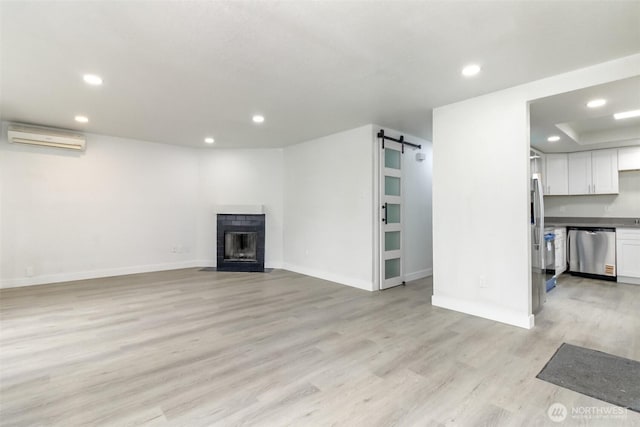 unfurnished living room featuring a wall mounted AC, light wood-style flooring, a fireplace, recessed lighting, and a barn door