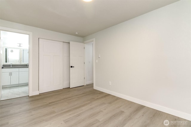 unfurnished bedroom featuring light wood finished floors, ensuite bath, baseboards, and a sink