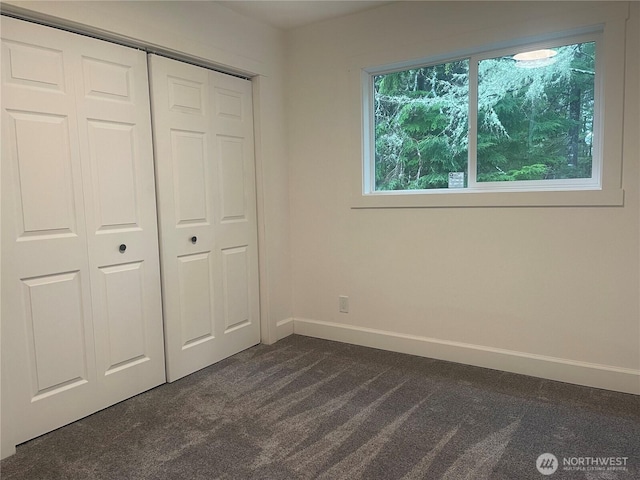 unfurnished bedroom with a closet, dark carpet, and baseboards