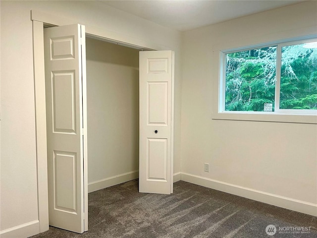 unfurnished bedroom featuring a closet, dark carpet, and baseboards