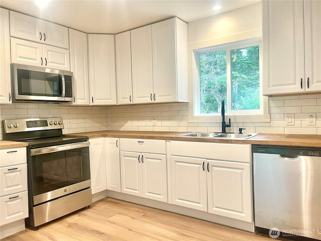 kitchen featuring white cabinets, wooden counters, stainless steel appliances, and a sink