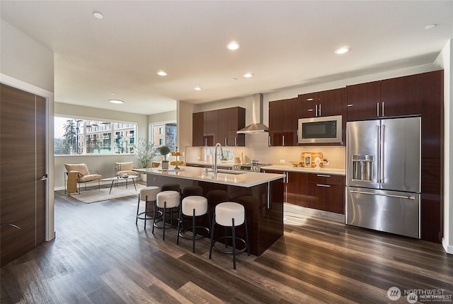 kitchen with a breakfast bar area, a sink, stainless steel appliances, light countertops, and wall chimney exhaust hood