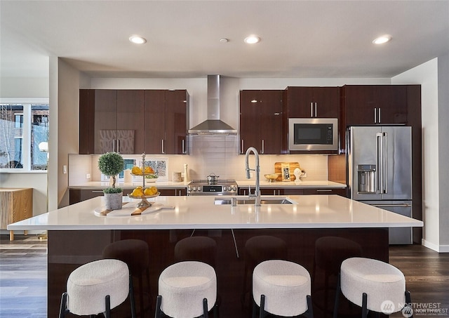 kitchen with light countertops, wall chimney range hood, appliances with stainless steel finishes, and a sink