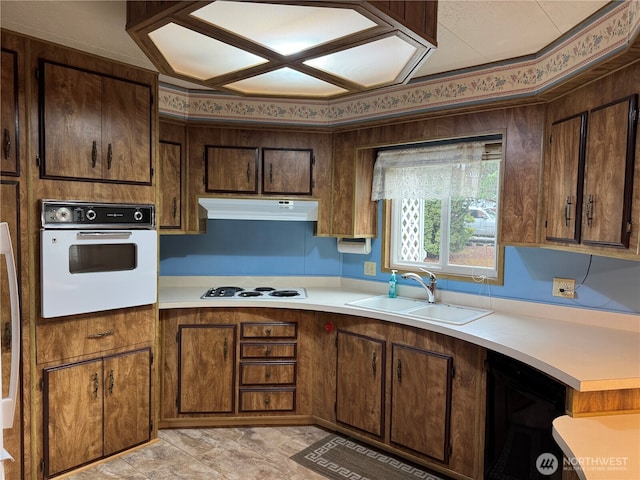 kitchen with light countertops, white appliances, a sink, and under cabinet range hood