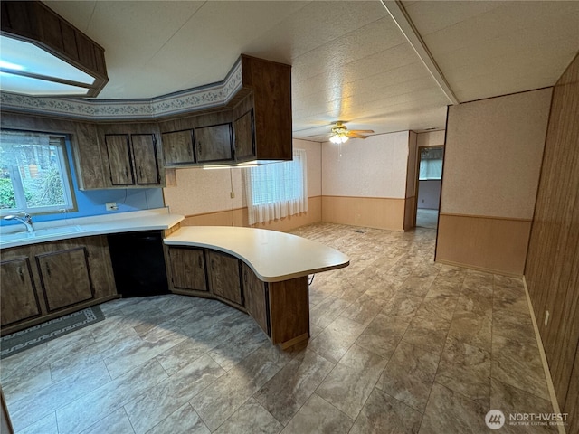 kitchen with black dishwasher, wainscoting, a peninsula, light countertops, and a sink