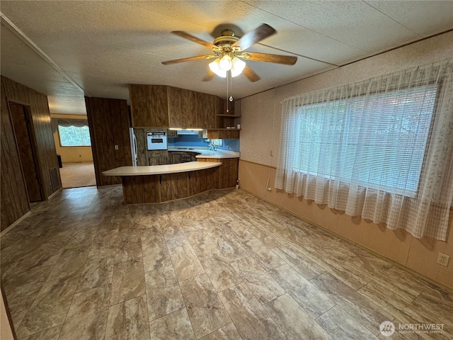 kitchen featuring ceiling fan, wall oven, a peninsula, light countertops, and stainless steel refrigerator