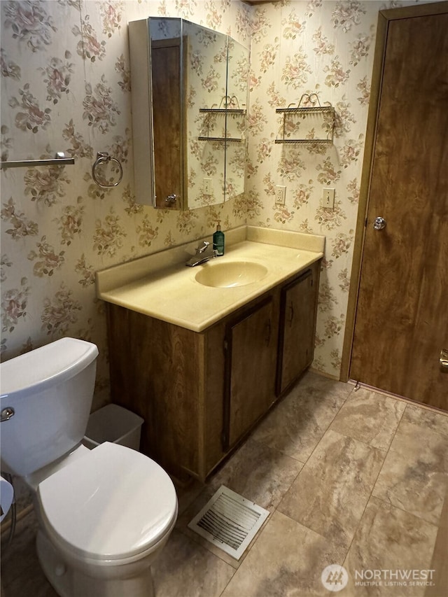 bathroom with visible vents, vanity, toilet, and wallpapered walls