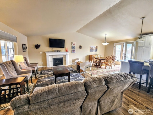 living room featuring french doors, a tiled fireplace, dark wood-type flooring, vaulted ceiling, and baseboards