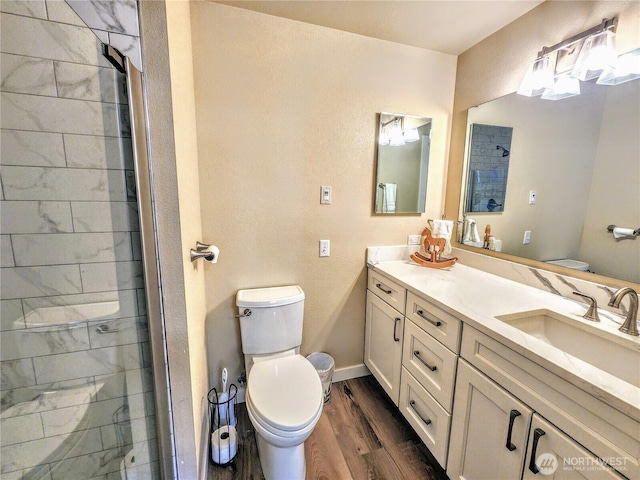 bathroom featuring double vanity, tiled shower, toilet, wood finished floors, and a sink