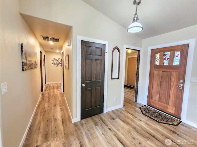 foyer entrance featuring light wood-style floors, visible vents, vaulted ceiling, and baseboards