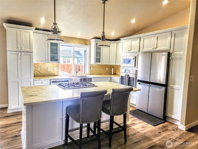 kitchen featuring vaulted ceiling, stainless steel appliances, wood finished floors, and light countertops