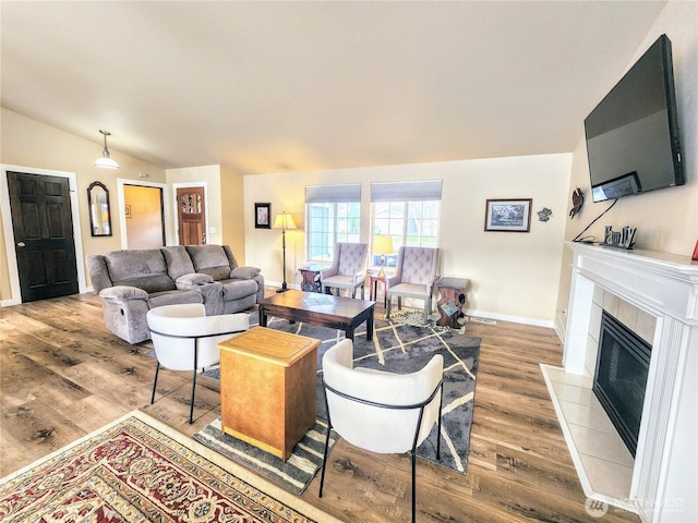 living room with vaulted ceiling, wood finished floors, a tile fireplace, and baseboards