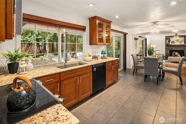 kitchen featuring brown cabinets, a sink, black dishwasher, a fireplace, and glass insert cabinets