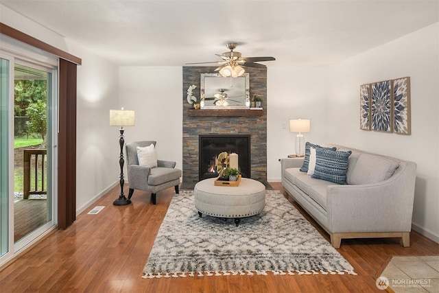 living area with wood finished floors, visible vents, baseboards, a fireplace, and ceiling fan