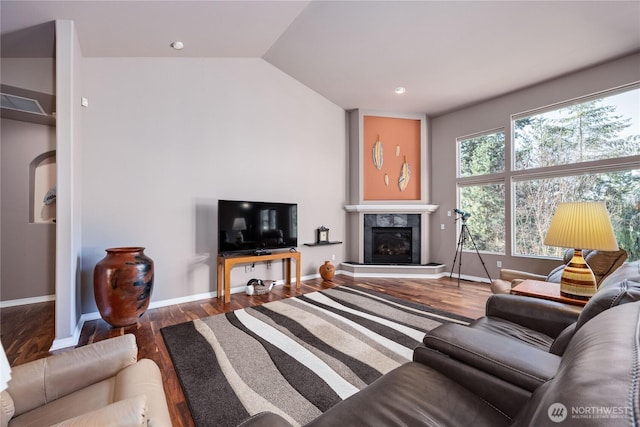 living area with lofted ceiling, a glass covered fireplace, baseboards, and wood finished floors