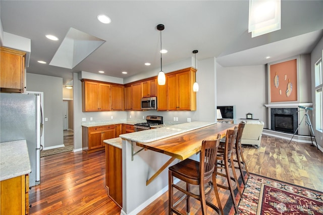 kitchen with recessed lighting, stainless steel appliances, a peninsula, brown cabinets, and dark wood finished floors