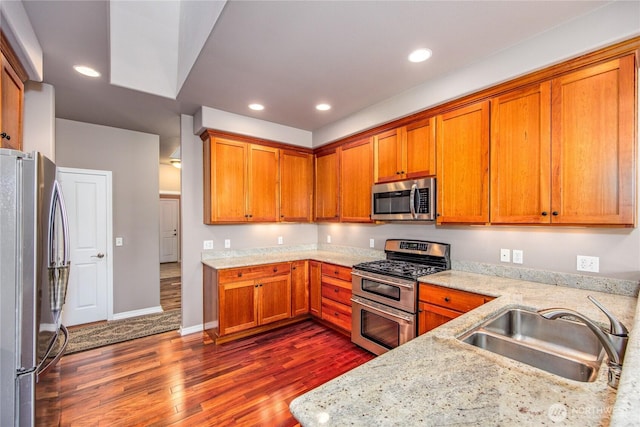 kitchen featuring recessed lighting, a sink, appliances with stainless steel finishes, dark wood-style floors, and brown cabinetry