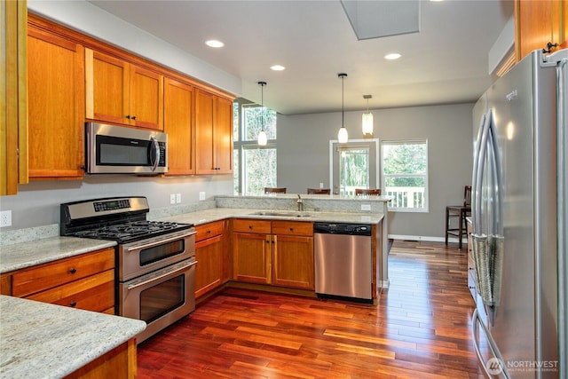 kitchen featuring a peninsula, appliances with stainless steel finishes, brown cabinetry, and a sink