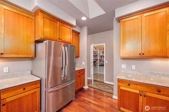 kitchen featuring a skylight, brown cabinets, dark wood finished floors, freestanding refrigerator, and baseboards