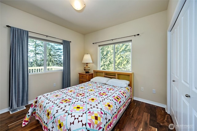 bedroom with a closet, visible vents, baseboards, and wood finished floors