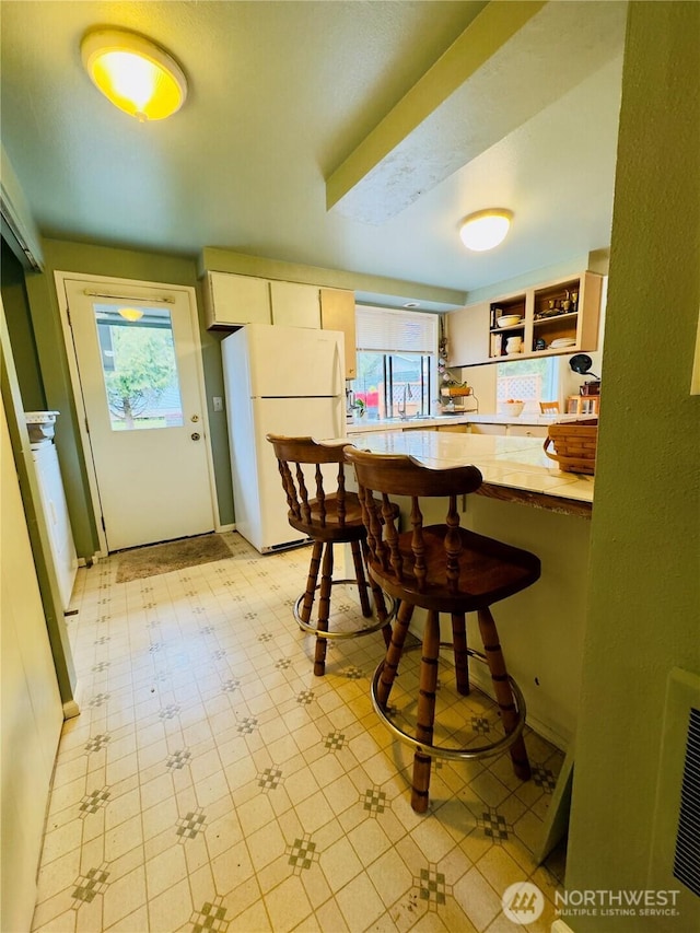 kitchen with light floors, a breakfast bar, light countertops, freestanding refrigerator, and open shelves