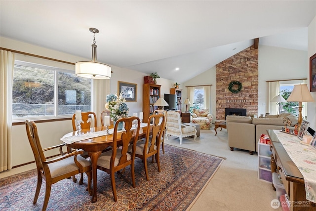 dining area with light colored carpet, vaulted ceiling, and a stone fireplace