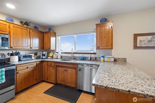 kitchen featuring light stone counters, brown cabinets, stainless steel appliances, a sink, and a peninsula