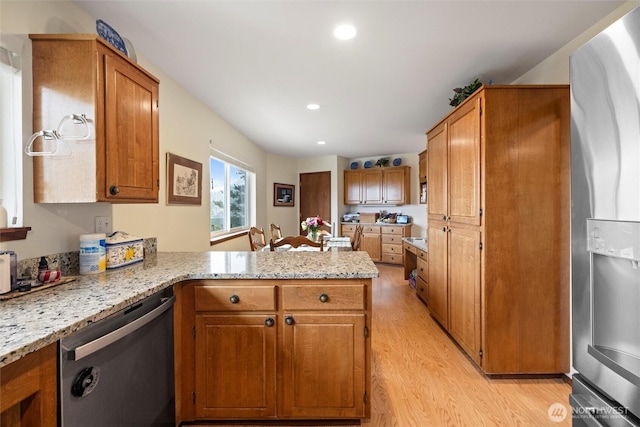 kitchen featuring light stone counters, light wood finished floors, stainless steel appliances, brown cabinetry, and a peninsula