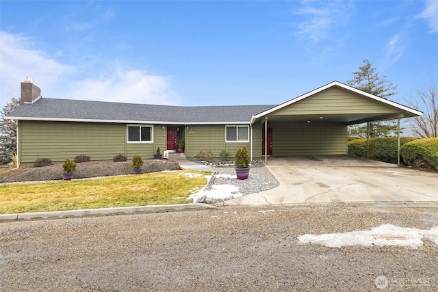 ranch-style home featuring concrete driveway, a chimney, an attached carport, roof with shingles, and a front yard