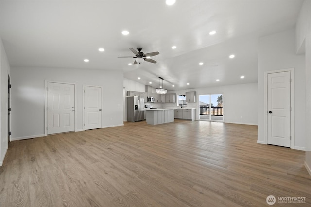 unfurnished living room with light wood-style floors, vaulted ceiling, baseboards, and a ceiling fan