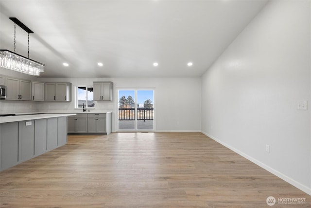 kitchen with pendant lighting, gray cabinets, light countertops, light wood-style floors, and a sink