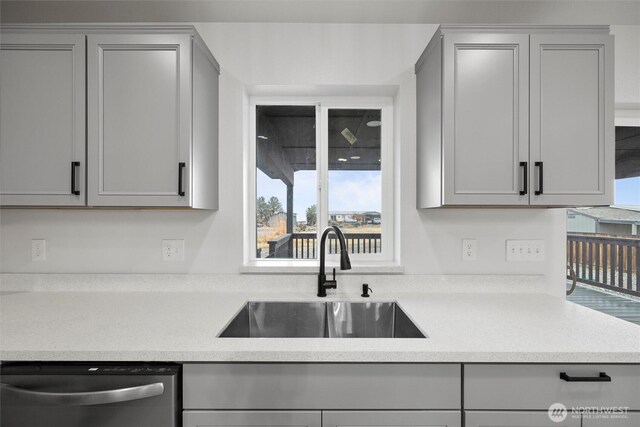 kitchen with gray cabinets, light countertops, dishwasher, and a sink