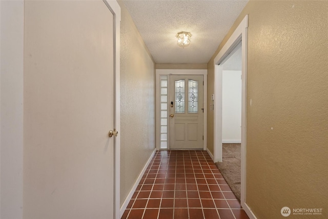 doorway featuring tile patterned floors, baseboards, a textured ceiling, and a textured wall